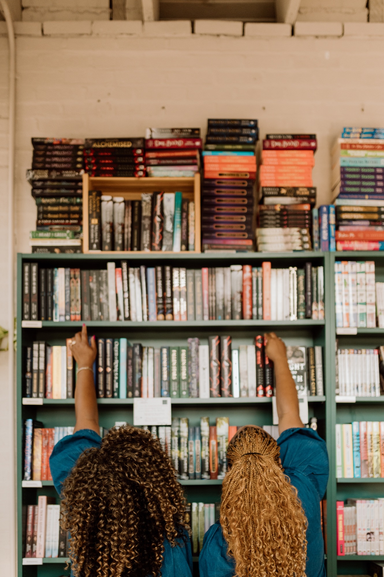 Tee and Tam reaching for books on a tall bookstore shelf