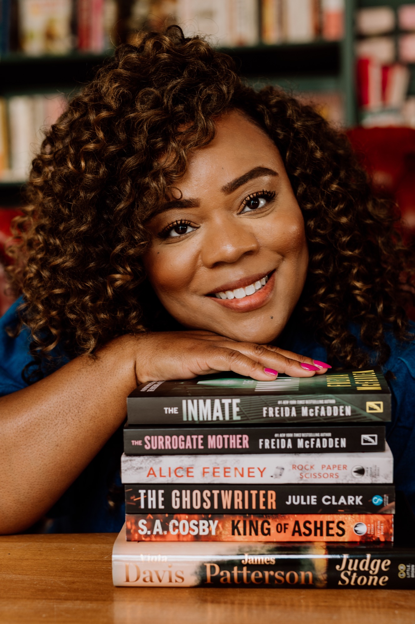 Tee smiling beside a stack of favorite books with The Inmate on top