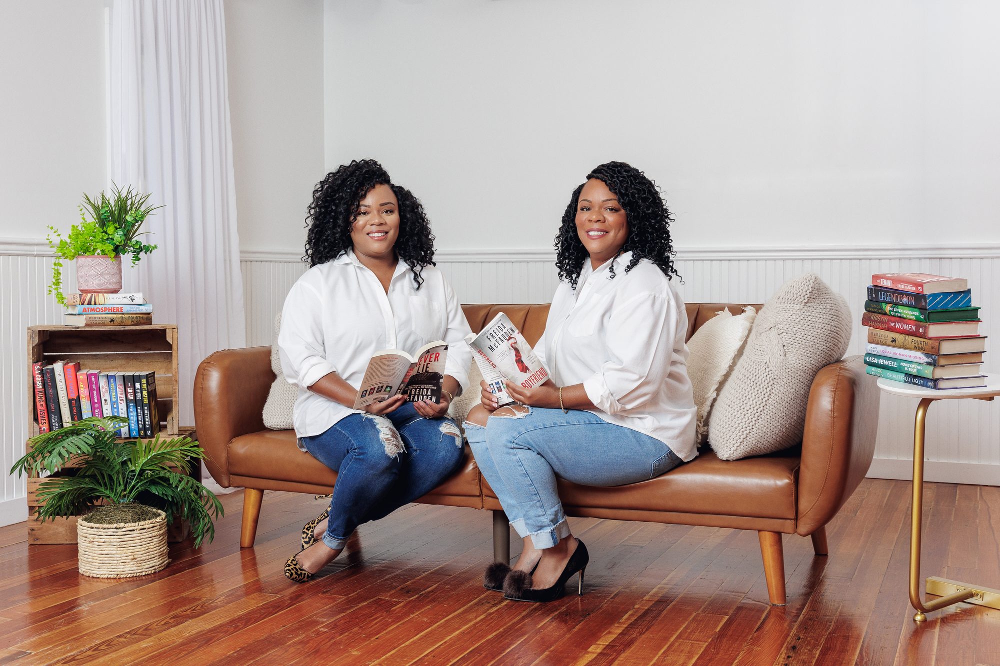 Tee and Tam reading thrillers together on a leather couch at home