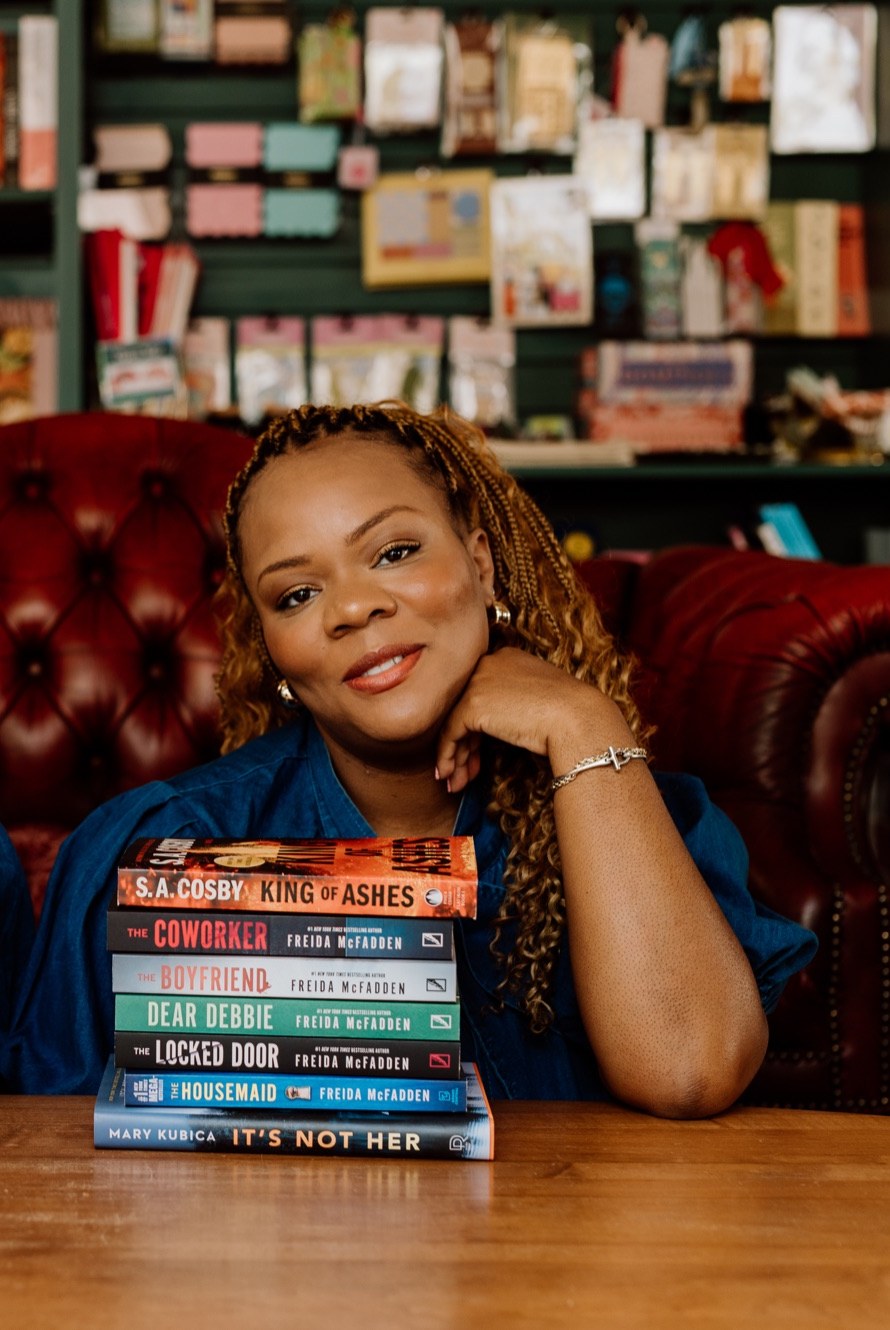 Tam smiling beside a stack of favorite books with S.A. Cosby’s King of Ashes on top